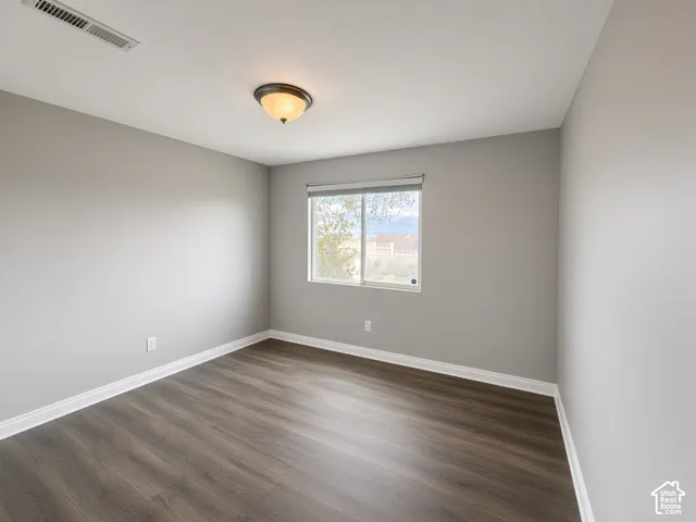 Neutral interior space featuring wood-finish flooring, light gray walls, a sliding window with a roller shade, and a semi-flush mount ceiling fixture