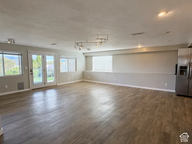 Open-concept interior featuring wood-finish flooring, glass-paned double doors, recessed lighting, and a built-in stainless steel refrigerator