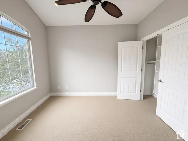 Room featuring an arched window, carpeted flooring, neutral wall paint, a ceiling fan, and a closet with integrated shelving