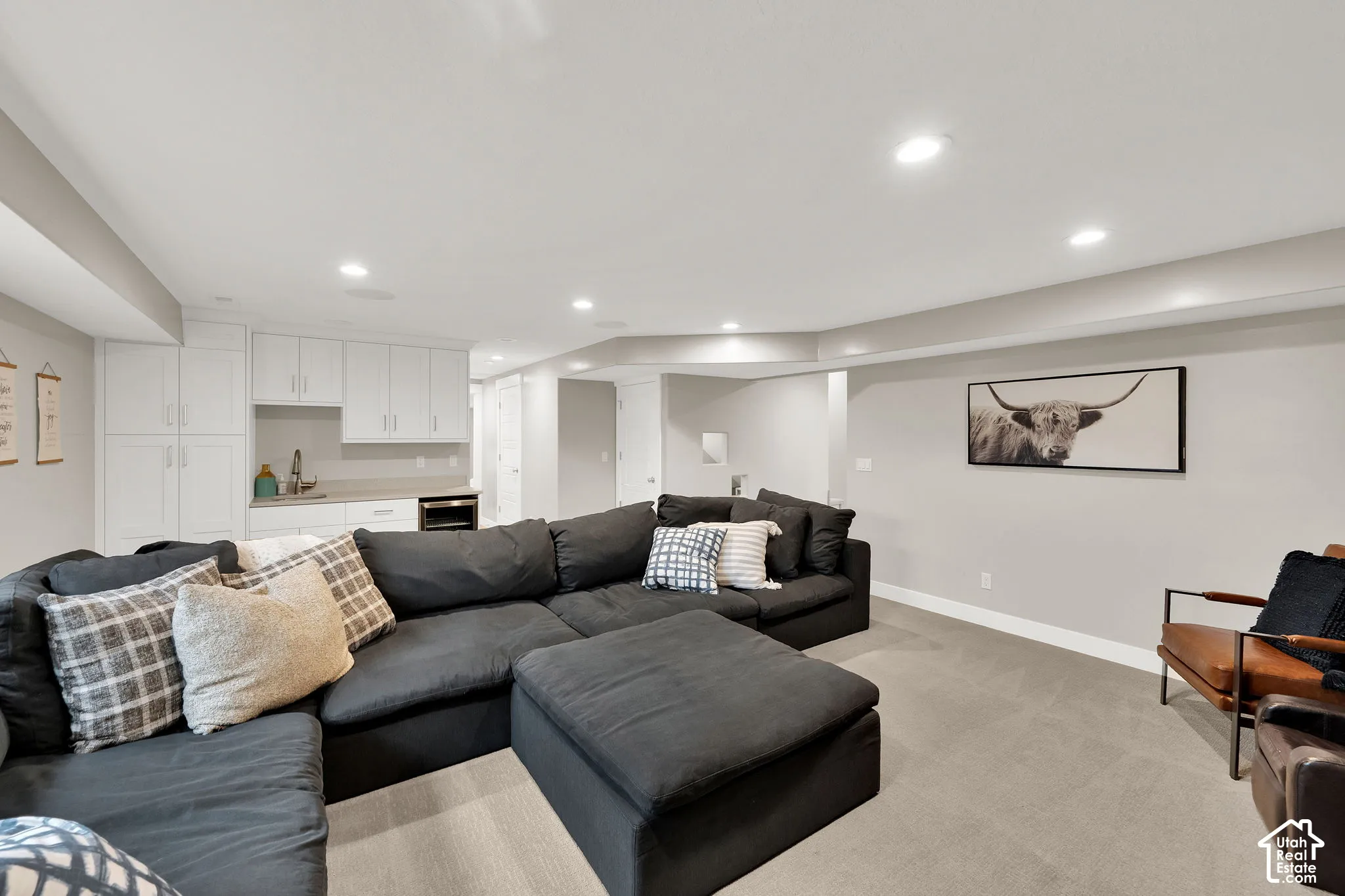 Recessed lighting, neutral wall palette, and built-in white cabinetry with a kitchenette area featuring a sink and under-counter appliance