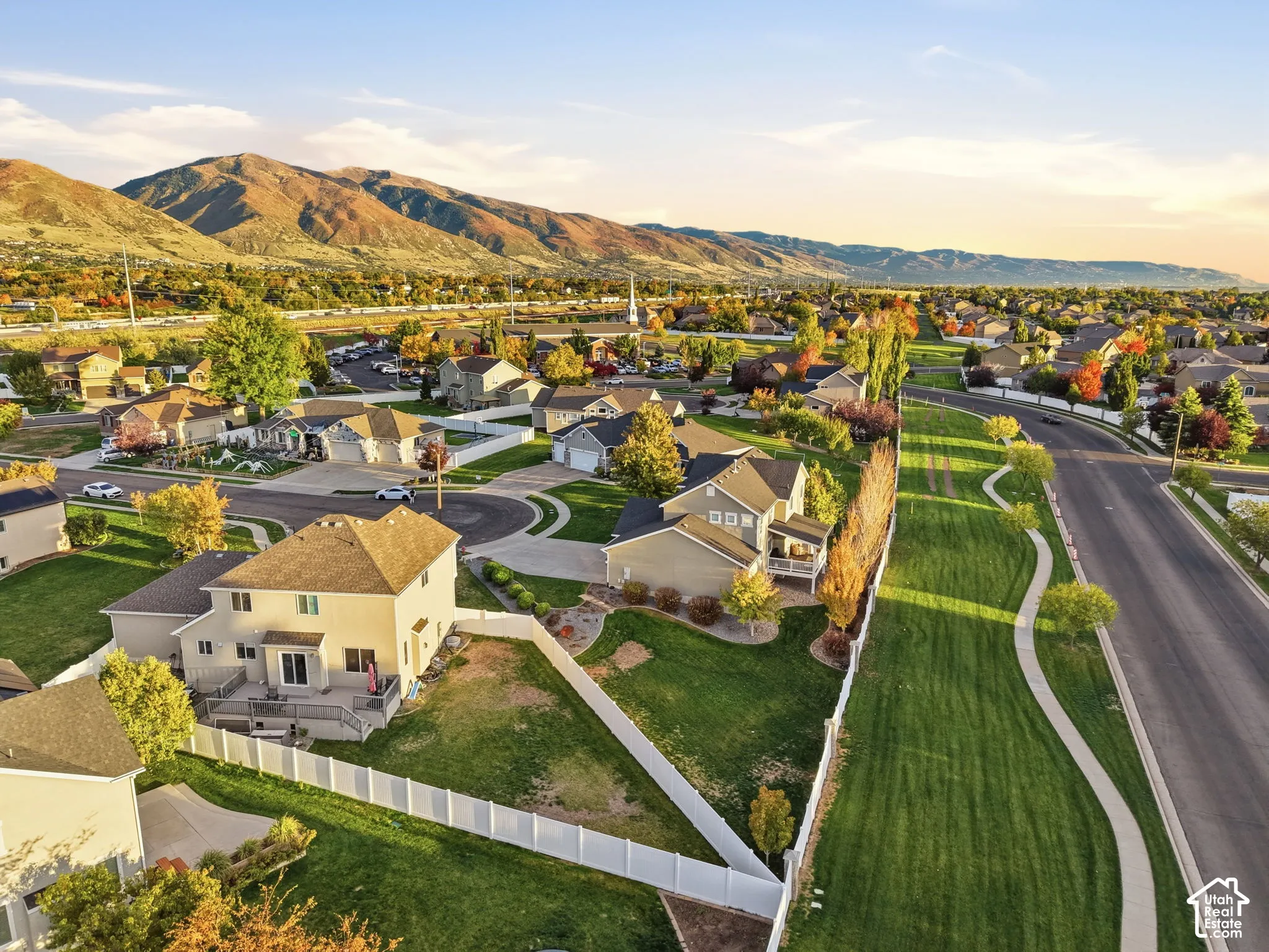 Aerial perspective featuring mountain backdrops, expansive manicured lawns, white vinyl fencing, and paved sidewalk paths