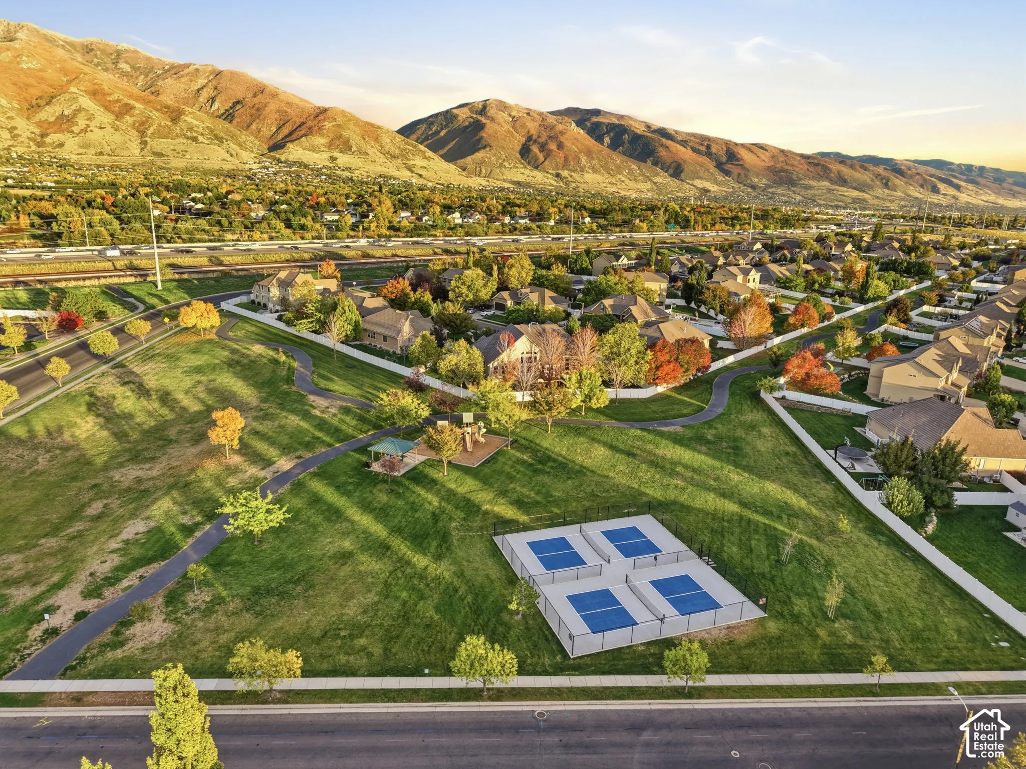 Expansive community grounds featuring four pickleball courts, paved walking paths, a covered pavilion, and mountain backdrop