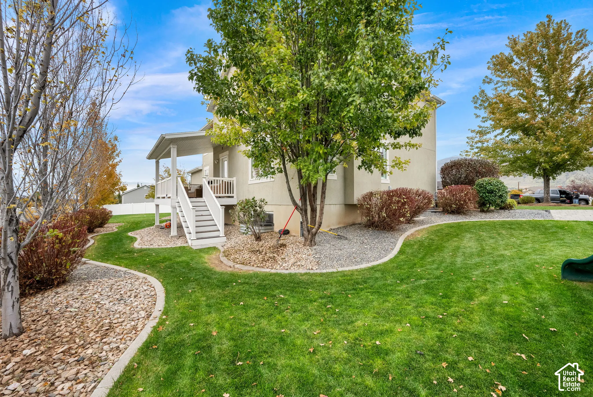 Exterior grounds featuring a raised covered deck, curved stone landscaping borders, mature trees, and a manicured lawn