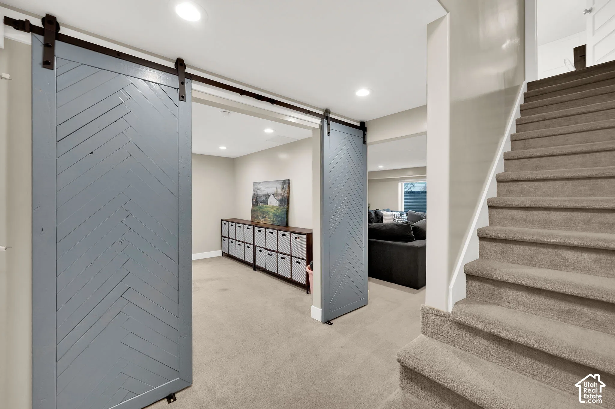 Dual blue-grey sliding barn doors featuring a herringbone pattern with matte black hardware, recessed lighting, and carpeted staircase