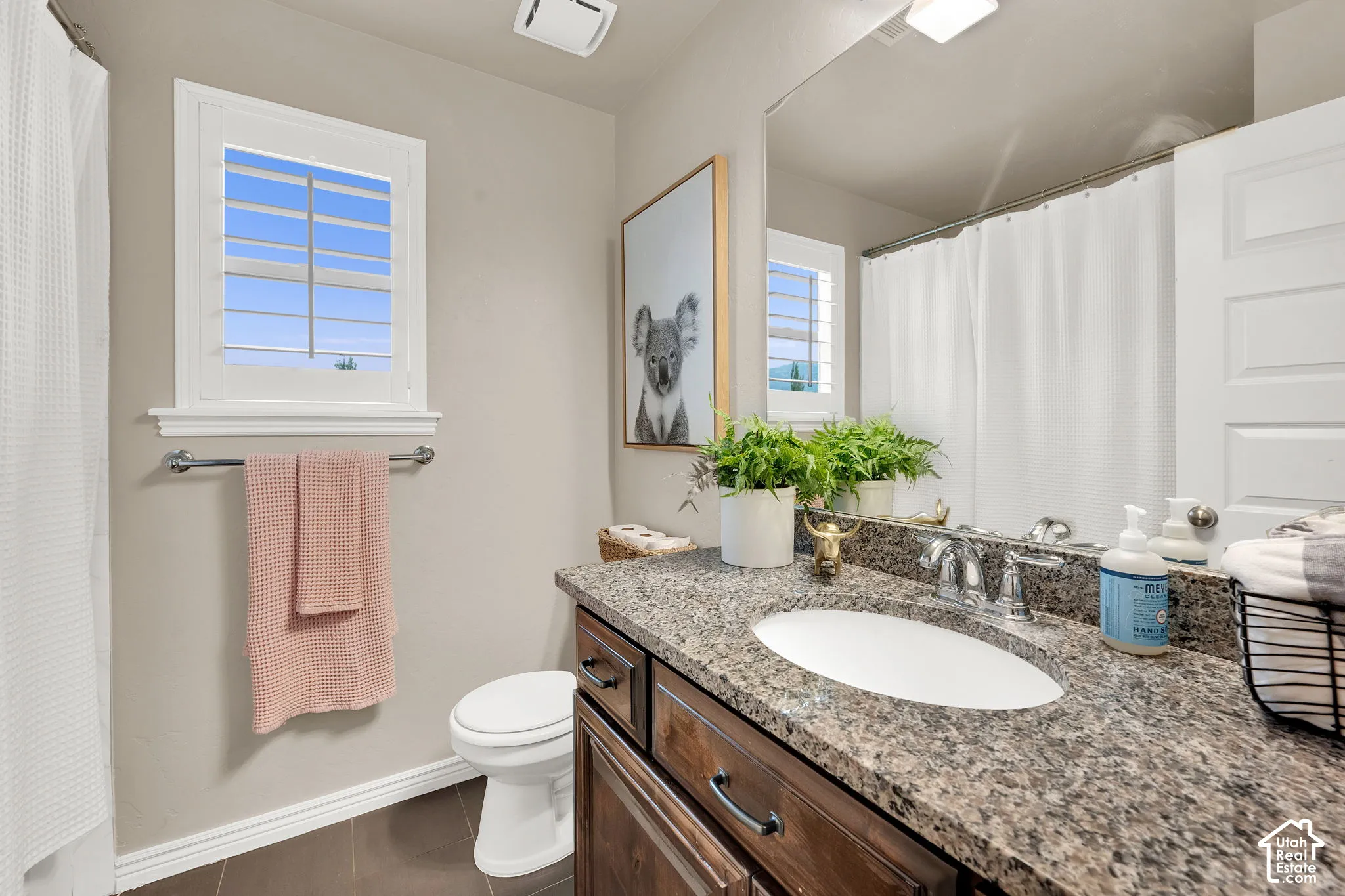 Bathroom featuring a stone-composite countertop, undermount sink, dark wood-finish cabinetry, a large wall-mounted mirror, and plantation shutters