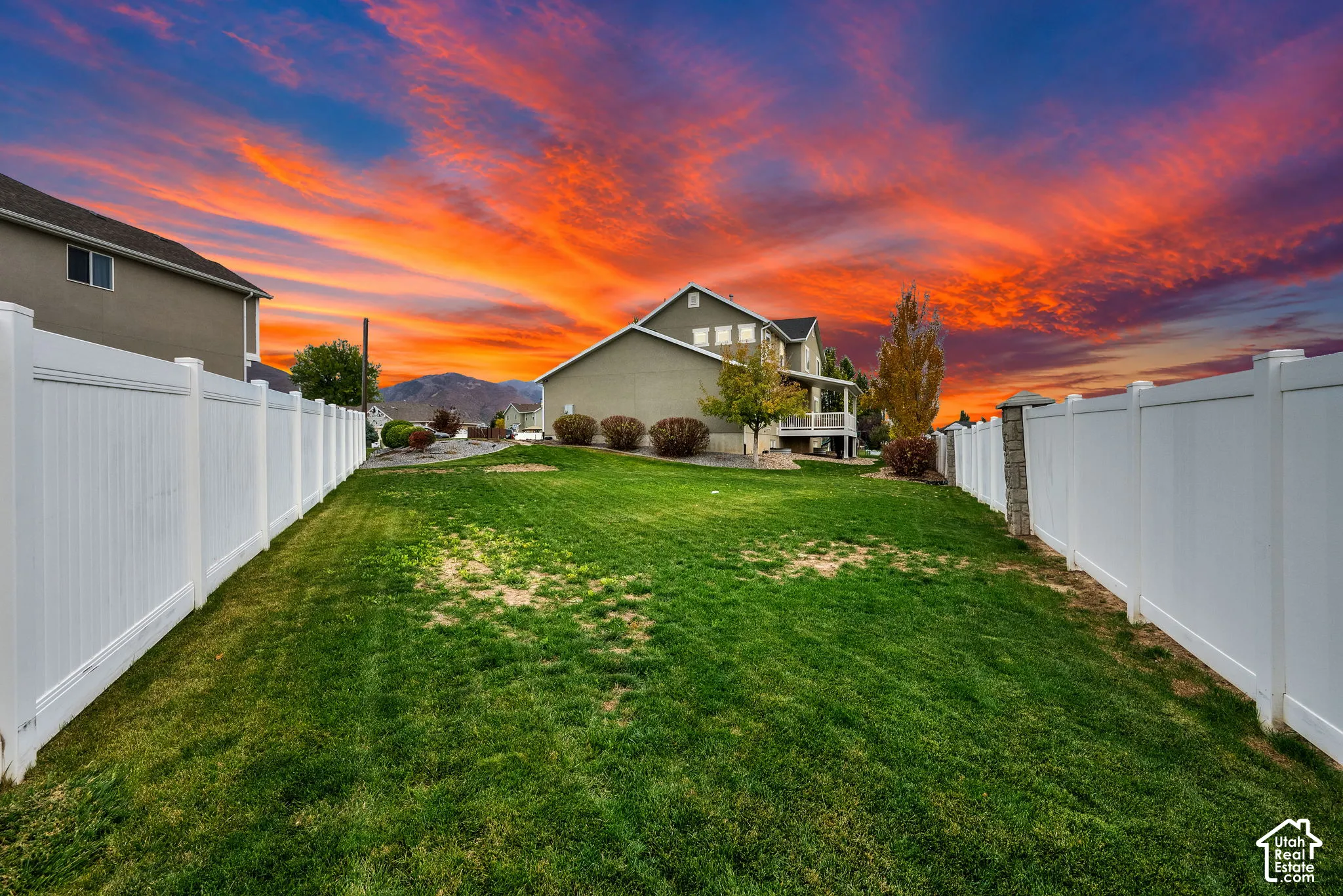 Rear yard featuring expansive lawn space, full-height white vinyl fencing, and mountain backdrop
