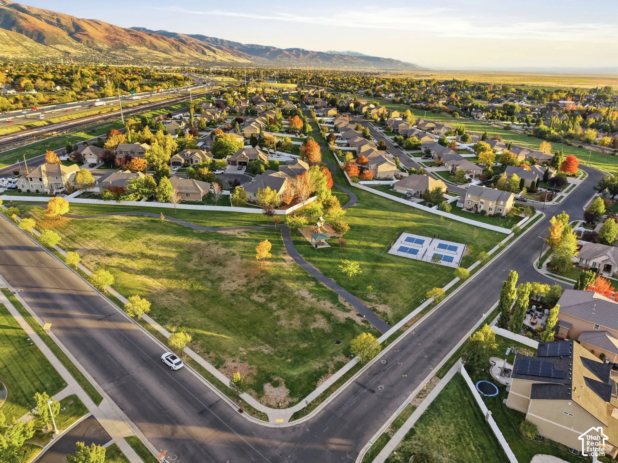 Aerial perspective showcasing expansive community green space, paved pedestrian pathways, dedicated recreation courts, mature landscaping, and a mountain backdrop
