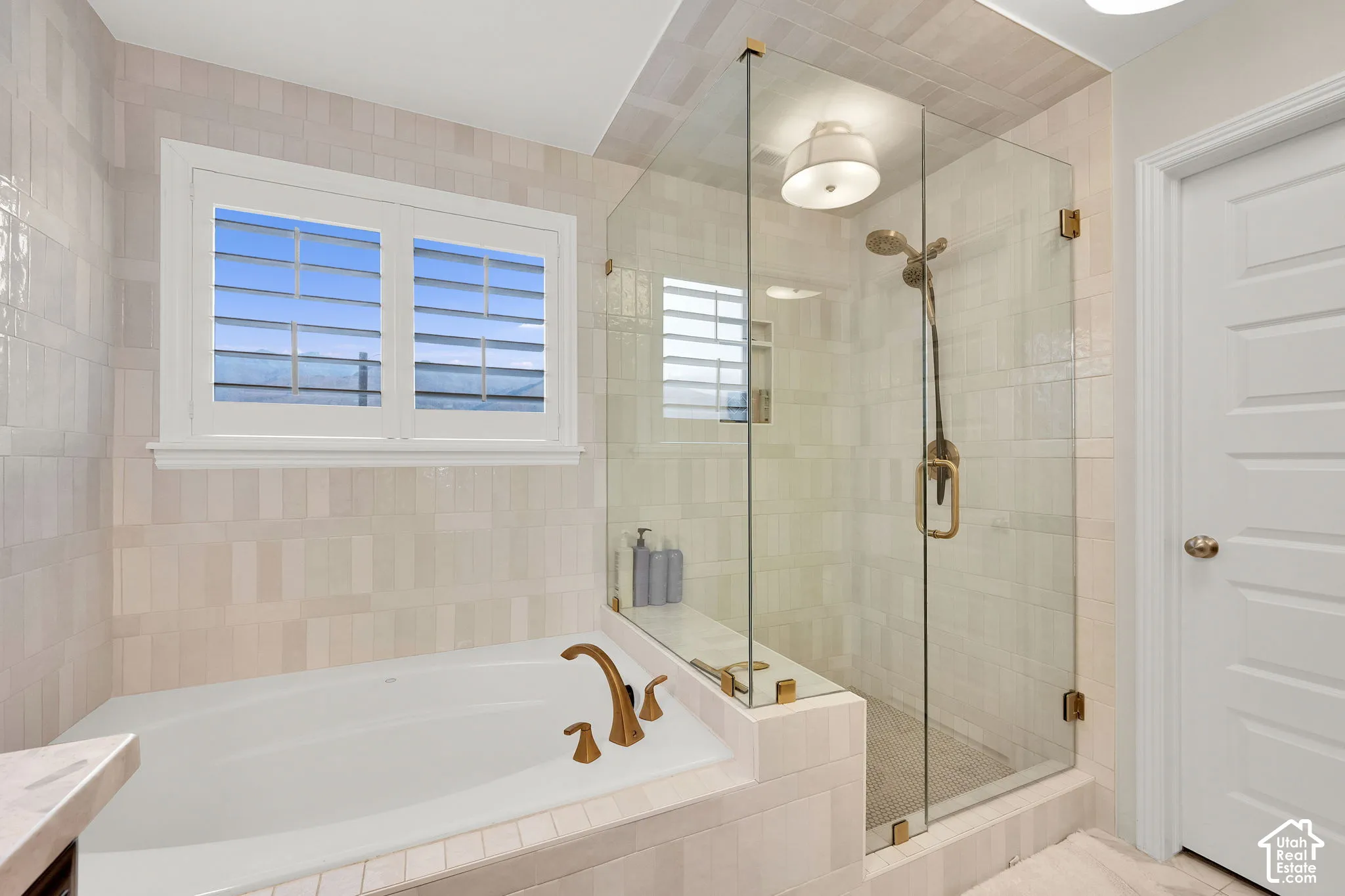 Soaking tub with brass-finish faucet, walk-in glass shower enclosure, brass-finish shower fixtures, and light-toned tile wall treatments