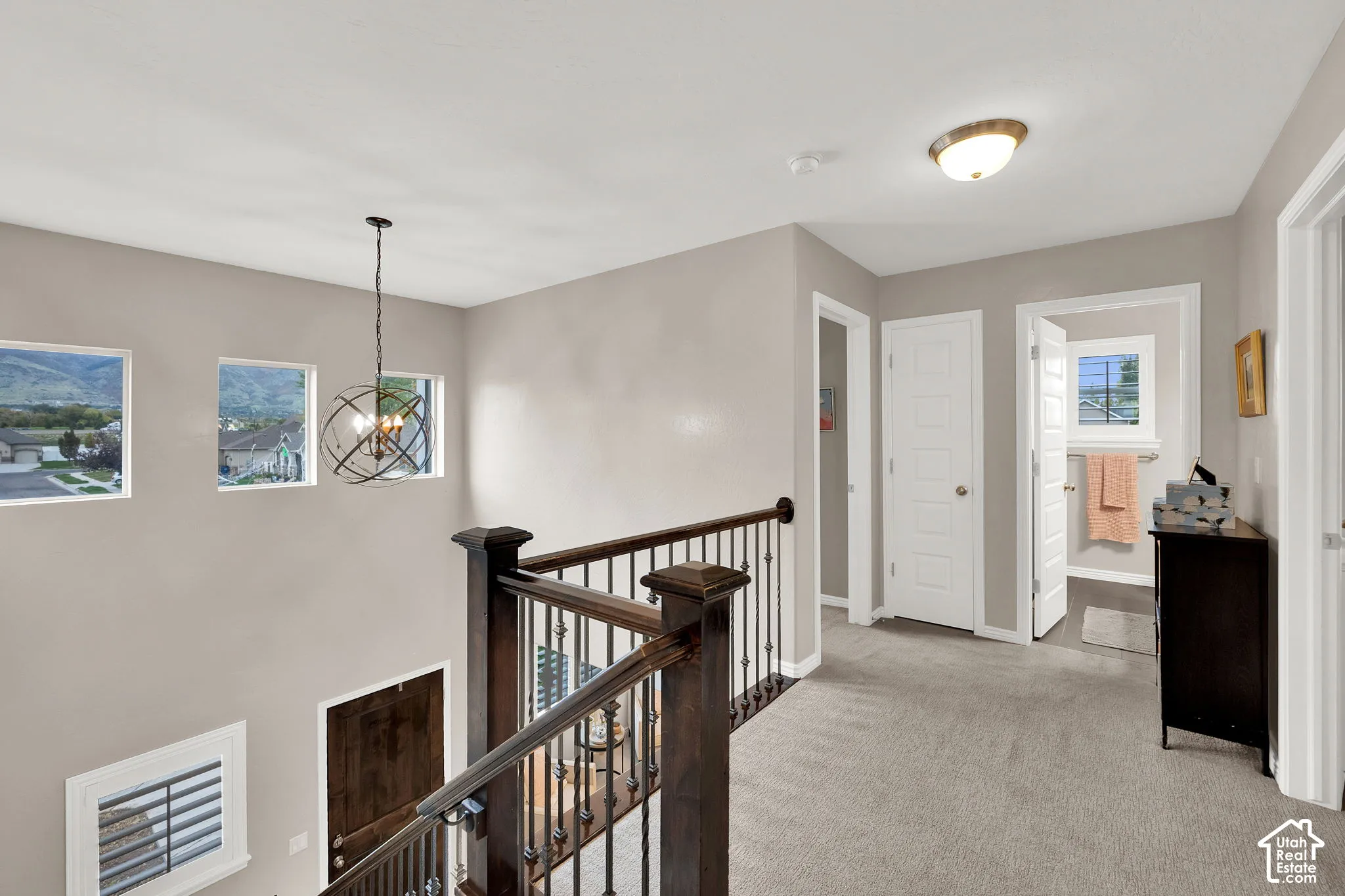 Landing featuring neutral carpeting, a metal orb-style pendant chandelier, and a wood banister with metal balusters