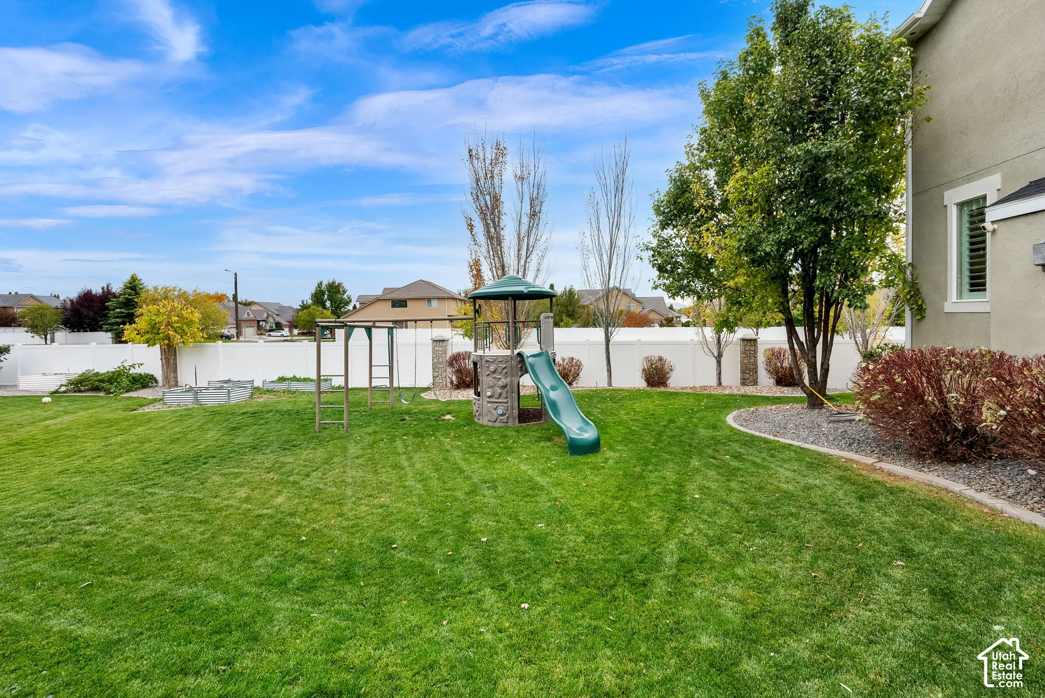 Expansive backyard featuring a grass lawn, mature trees, ornamental landscaping, and a perimeter vinyl privacy fence