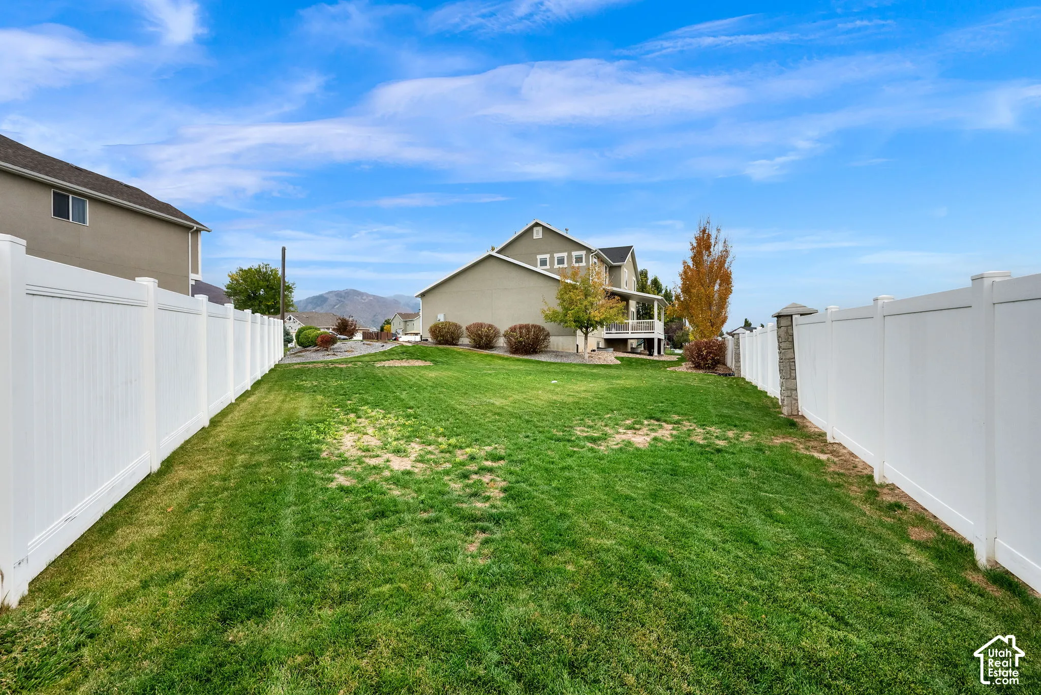 Backyard featuring a sprawling lawn, full-perimeter white vinyl fencing, and mature landscaping