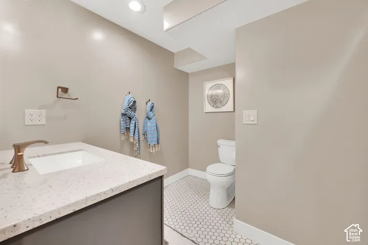 Powder room featuring a vanity with a light-toned speckled countertop, recessed rectangular sink, bronze-tone faucet, and hexagonal floor tile