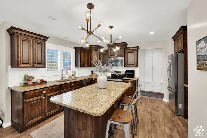 Kitchen featuring stained wood cabinetry, stone countertops, central island, dual geometric light fixtures, and white tiled backsplash