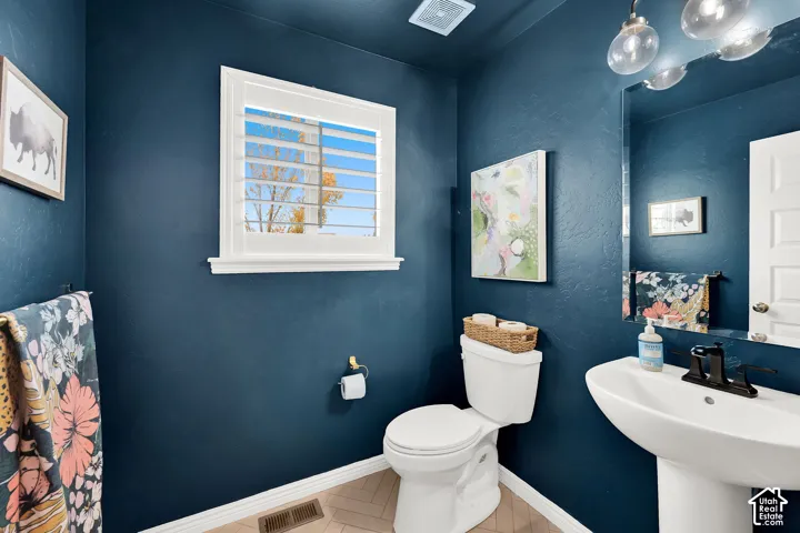 Powder room featuring a pedestal sink, matte black faucet, herringbone-patterned flooring, and plantation shutters