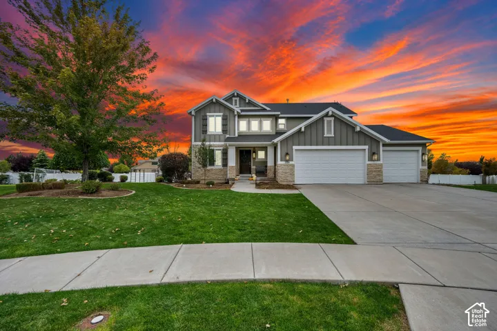Two-story residence featuring vertical and horizontal siding, stone veneer accents, a three-car garage, and a manicured lawn