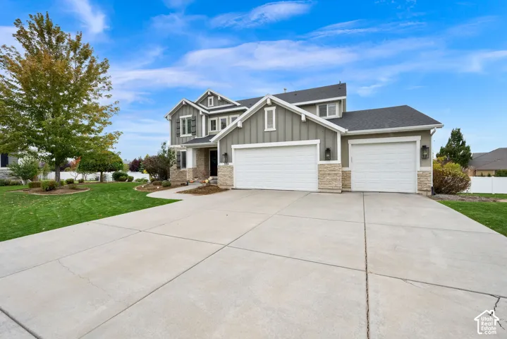 Two-story exterior featuring board-and-batten siding, stone veneer accents, a three-car garage, and a concrete driveway