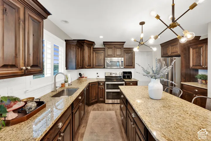 Kitchen featuring stained wood cabinetry, stone-surface countertops, central island, stainless steel appliances, and a multi-arm geometric light fixture