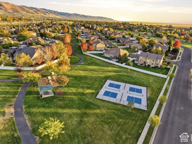 Aerial perspective of a community green space featuring multi-use athletic courts, a covered pavilion, paved walking paths, and mountain scenery