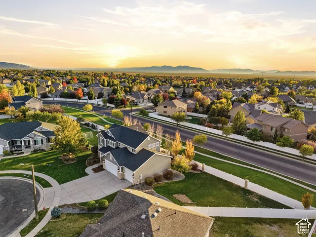 Aerial perspective of a multi-story residence with a multi-car garage, concrete driveway, and expansive lawn area enclosed by white vinyl fencing