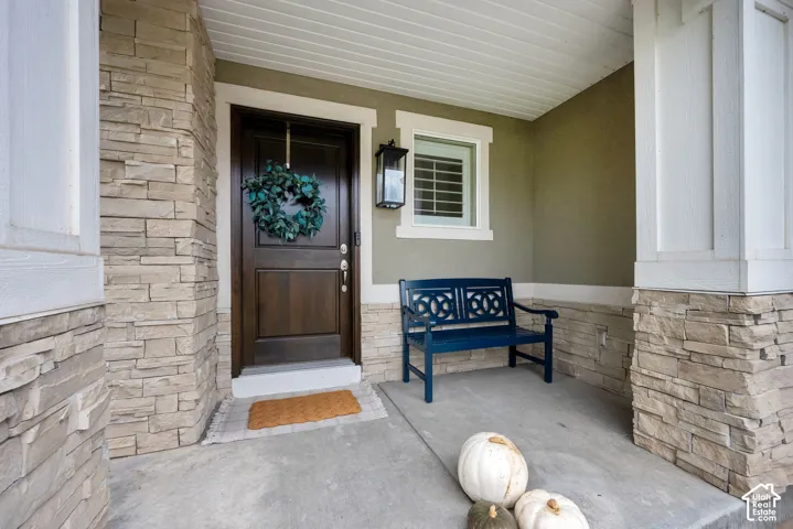 Covered front entry featuring stone veneer accents, square support columns, solid wood-finish entry door, and wall-mounted exterior lighting