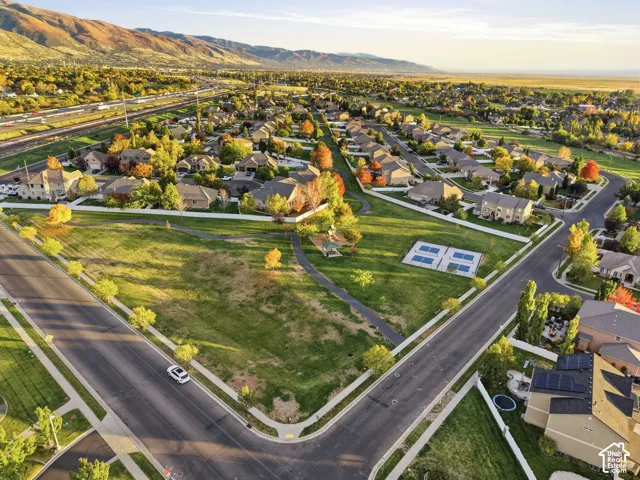 Aerial perspective showcasing expansive community green space, paved pedestrian pathways, dedicated recreation courts, mature landscaping, and a mountain backdrop