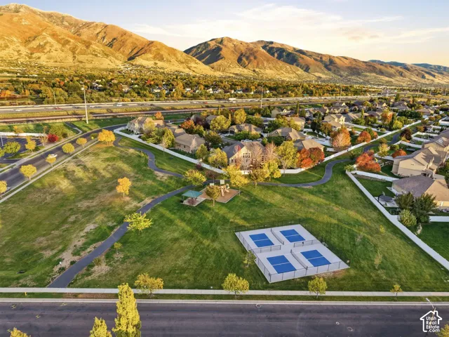 Extensive park area featuring paved walking paths, a playground, tennis courts, and mature trees against a mountain backdrop