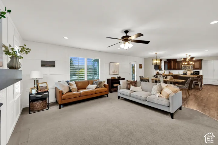 Living area featuring grid-pattern wall molding, recessed lighting, and a ceiling fan, opening to a kitchen equipped with dark wood cabinetry and wood-finish flooring