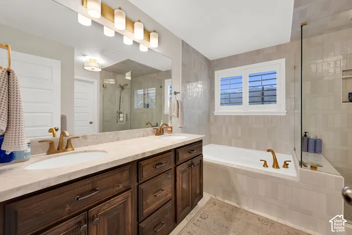 Dual-sink vanity with stone countertop and brass-finish fixtures, inset soaking tub with tile surround, and frameless glass shower enclosure