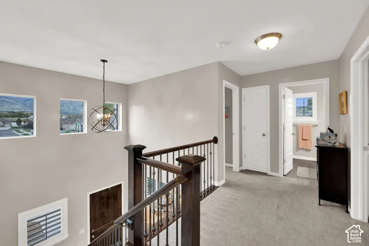 Landing featuring neutral carpeting, a metal orb-style pendant chandelier, and a wood banister with metal balusters