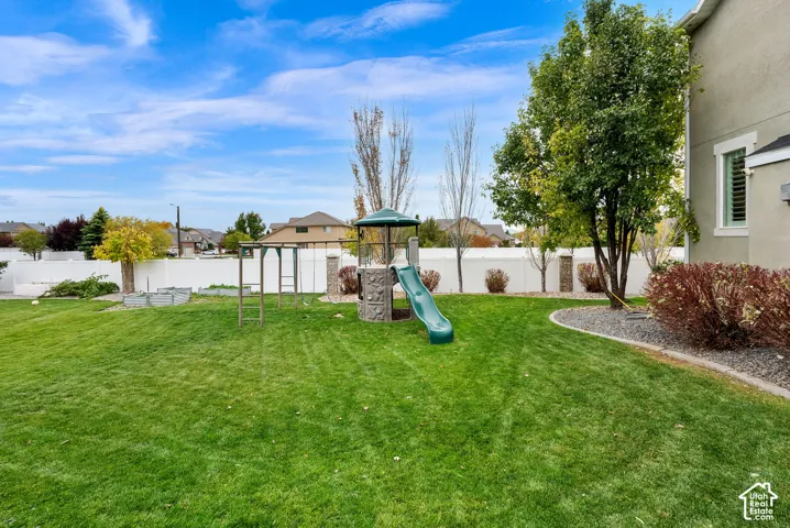 Expansive backyard featuring a grass lawn, mature trees, ornamental landscaping, and a perimeter vinyl privacy fence