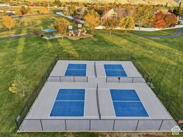 Fenced pickleball complex with four courts, surrounded by manicured grass lawns and mature trees