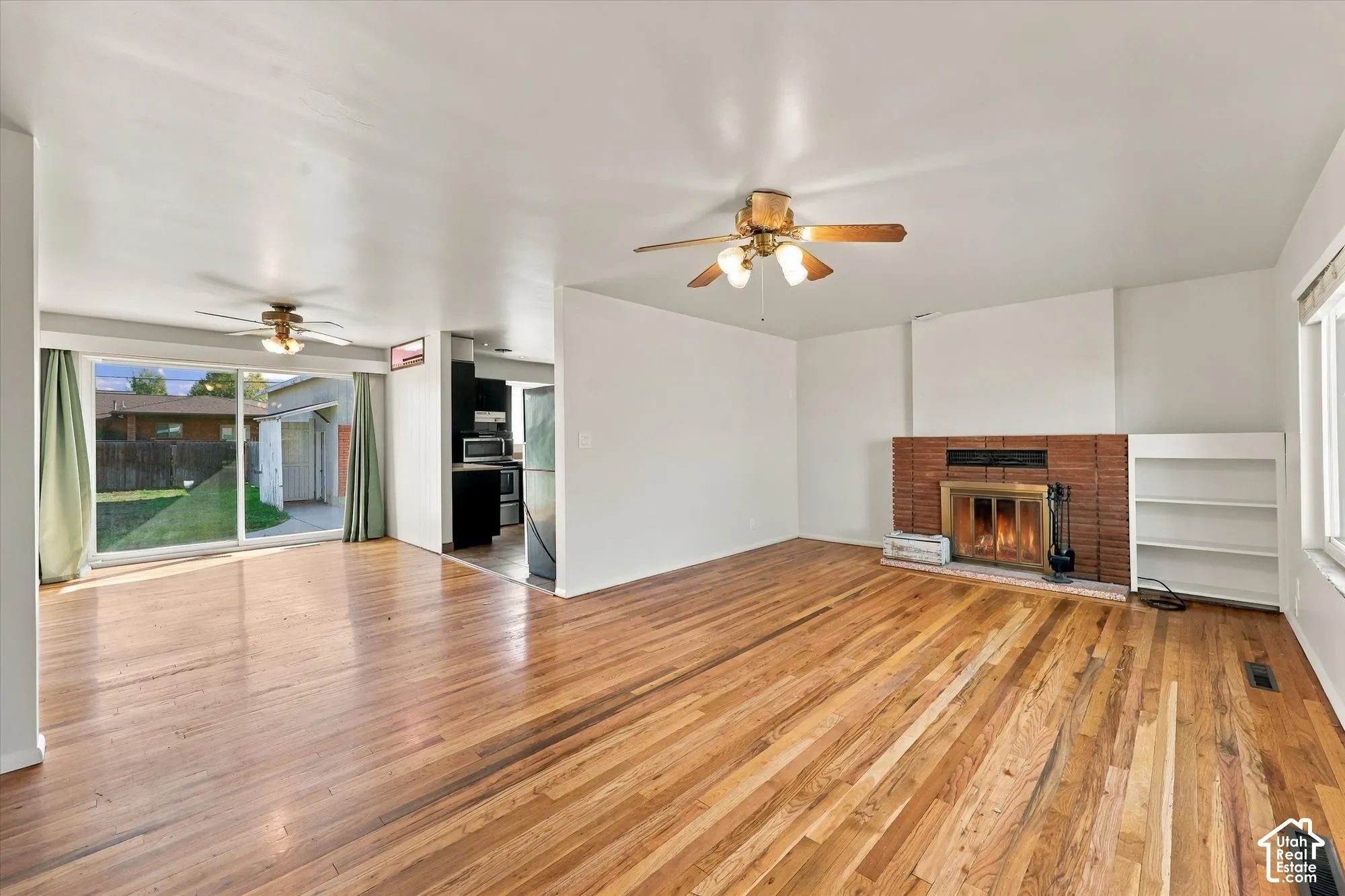 Interior space featuring wood-finish flooring, a floor-to-ceiling brick fireplace with a metal insert, built-in shelving, two ceiling fans, and a large sliding glass door