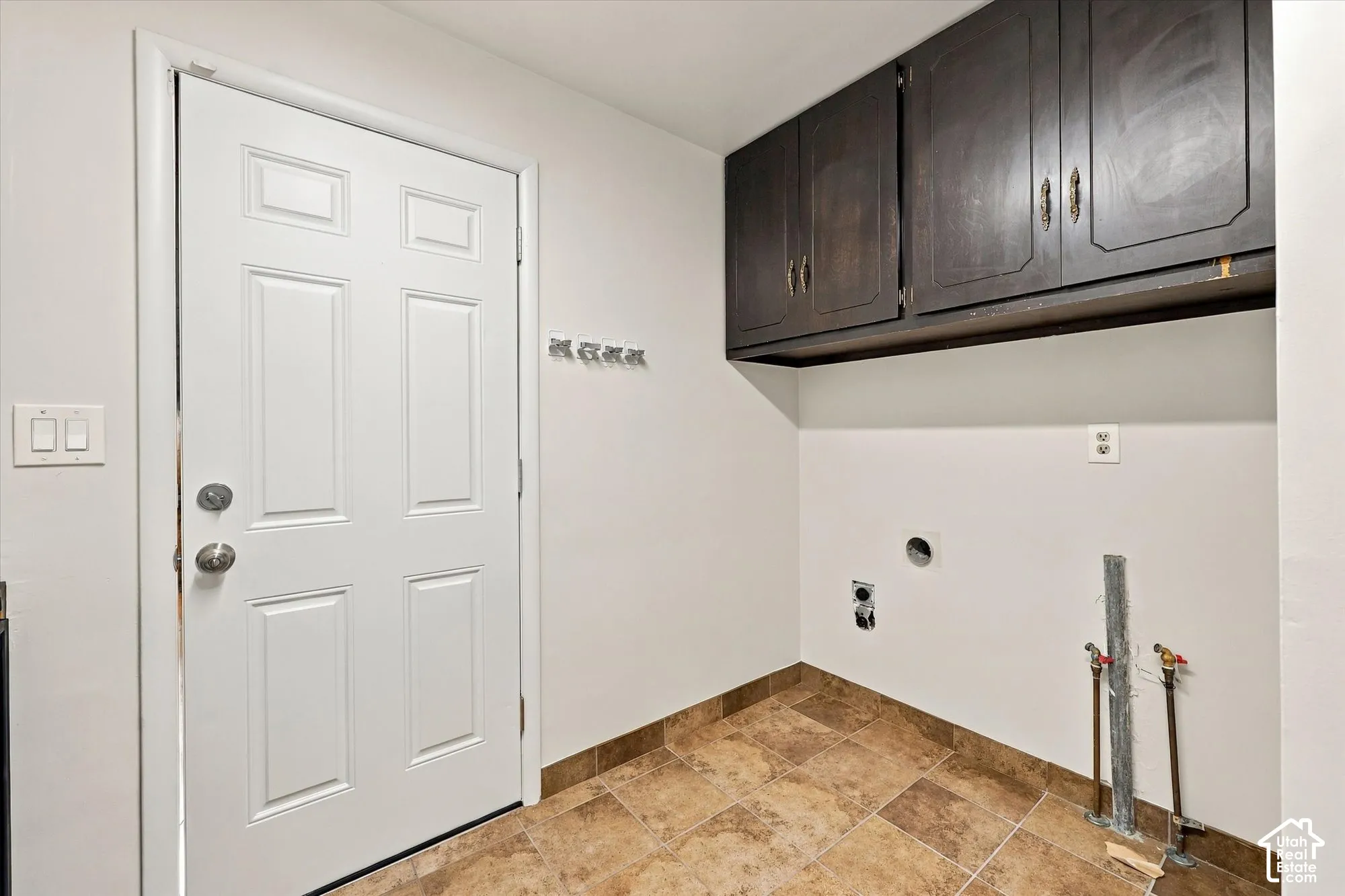 Utility area featuring dark wood-finish wall cabinetry, stone-texture tile flooring, a metal multi-hook rack, and washer and dryer utility hookups