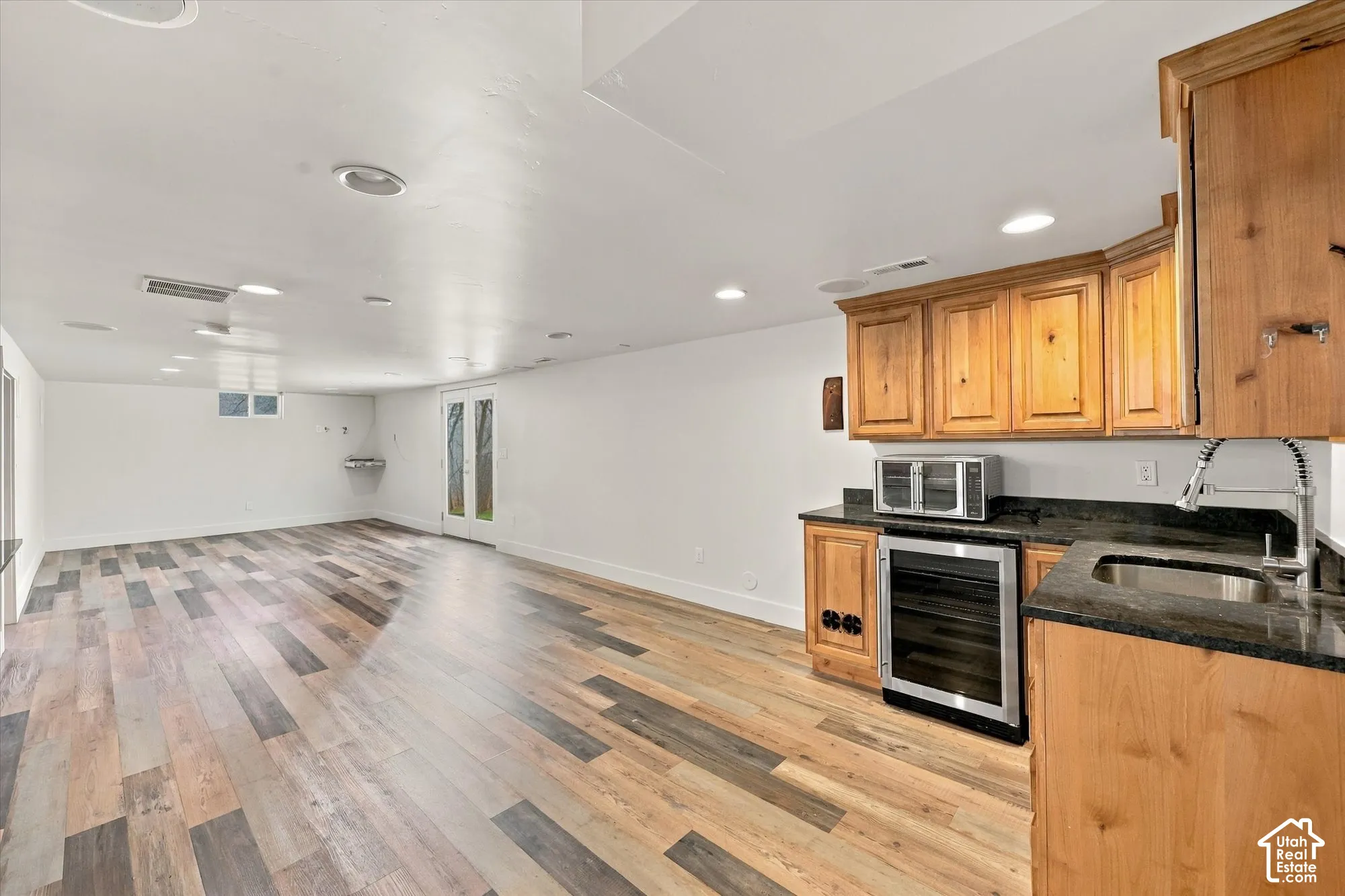 Multi-purpose area featuring wood-finish flooring, recessed lighting, a wet bar with stone countertops, and full-glass panel doors