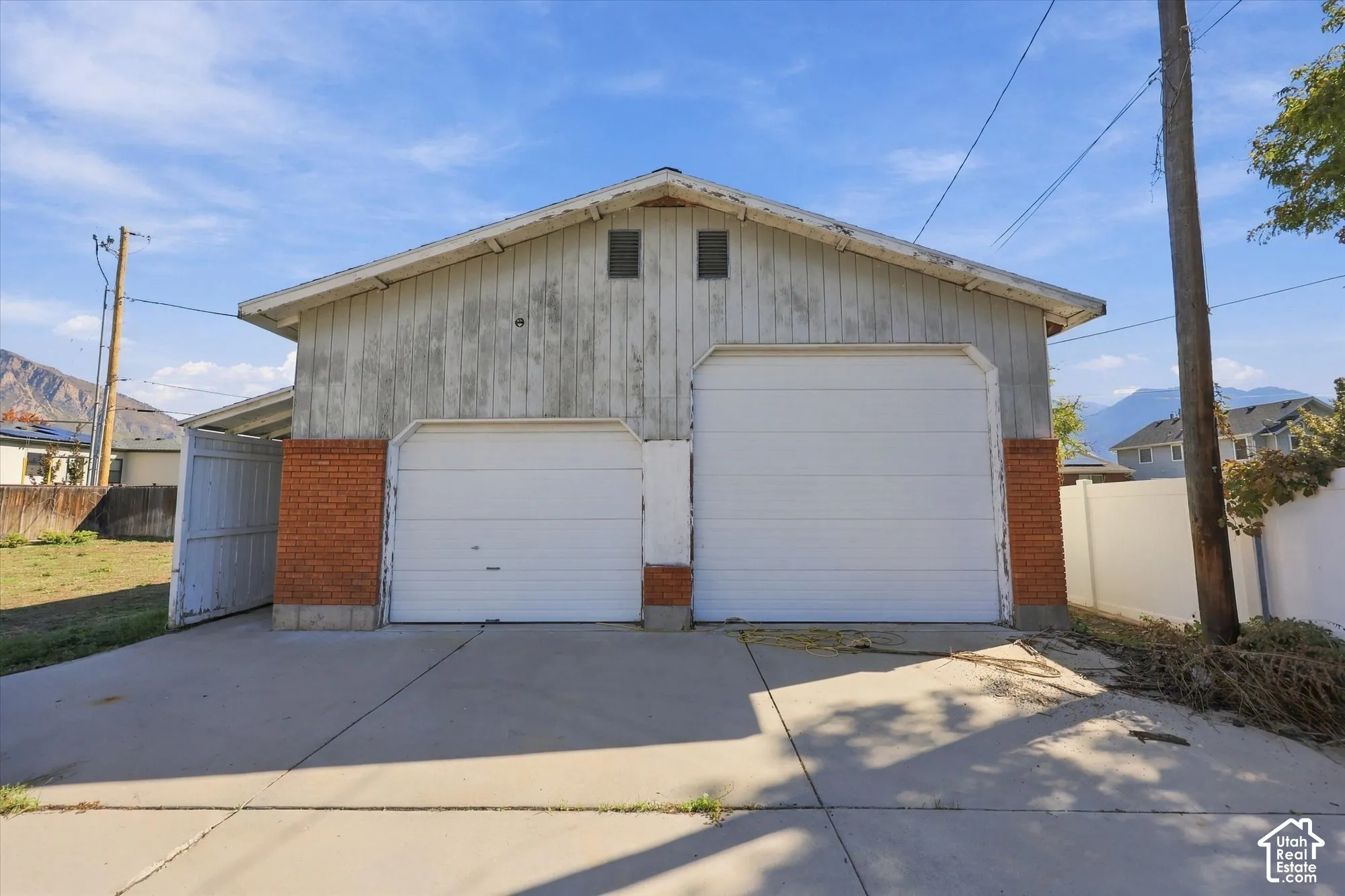 Detached two-car garage featuring vertical wood siding, brick masonry detailing, concrete driveway, and covered side storage area