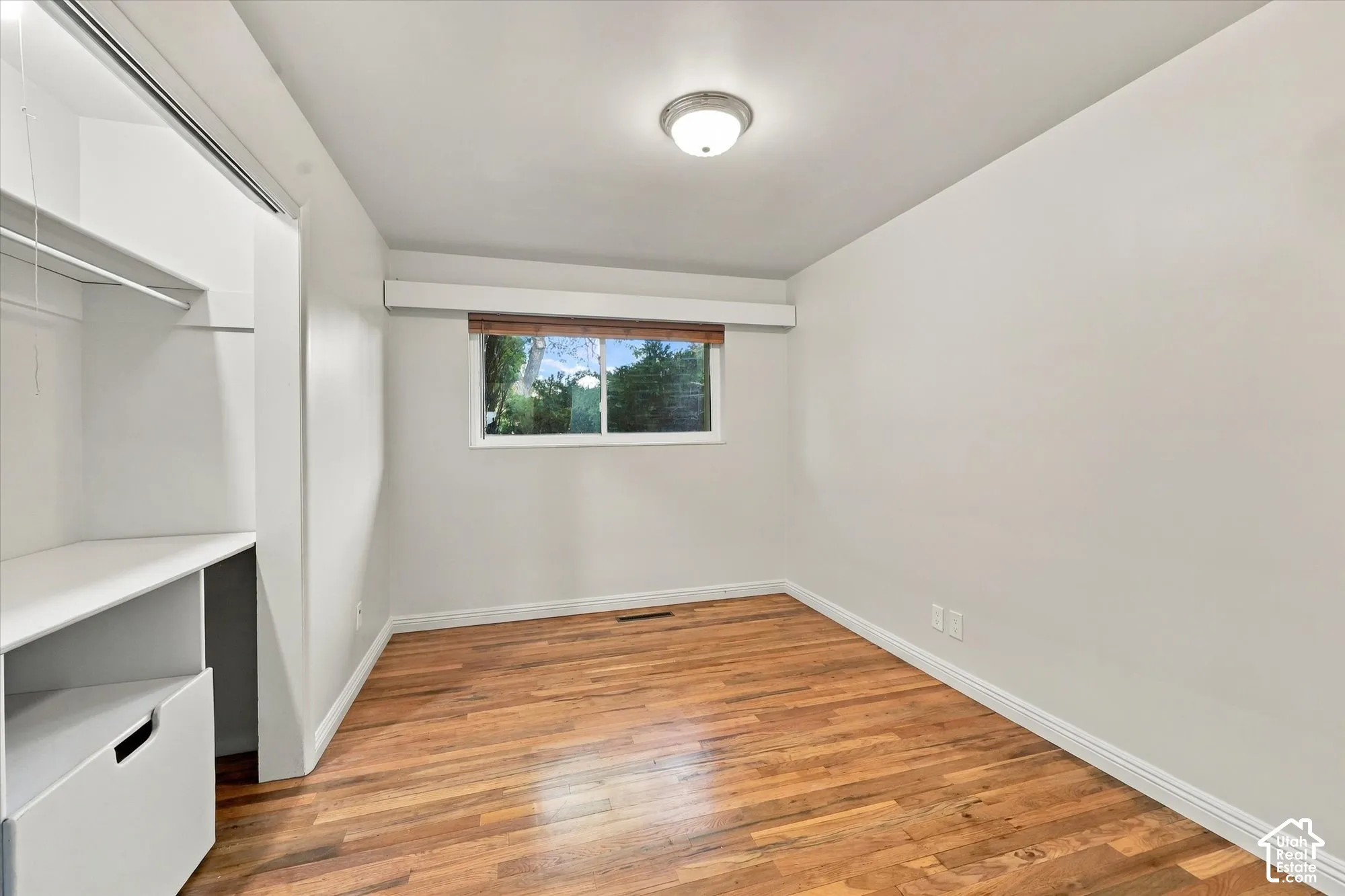 Wood-finish flooring, sliding window with a window valance, ceiling-mounted light fixture, and closet with built-in shelving