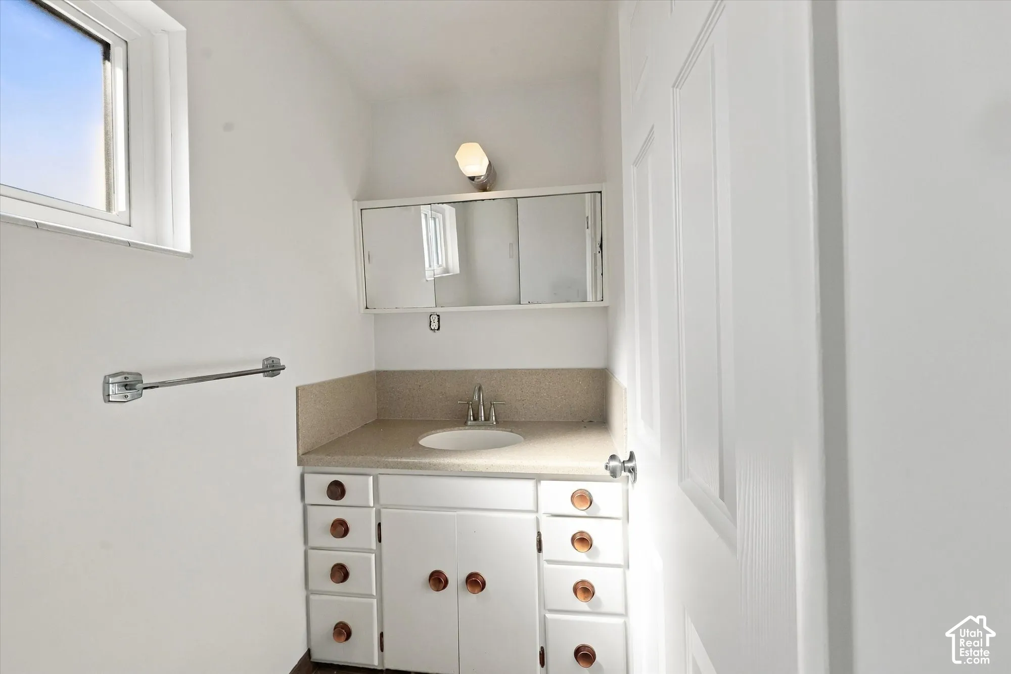 Bathroom vanity featuring white cabinetry, a solid-surface countertop with an integrated basin, a three-panel mirrored medicine cabinet, and wall-mounted light fixture