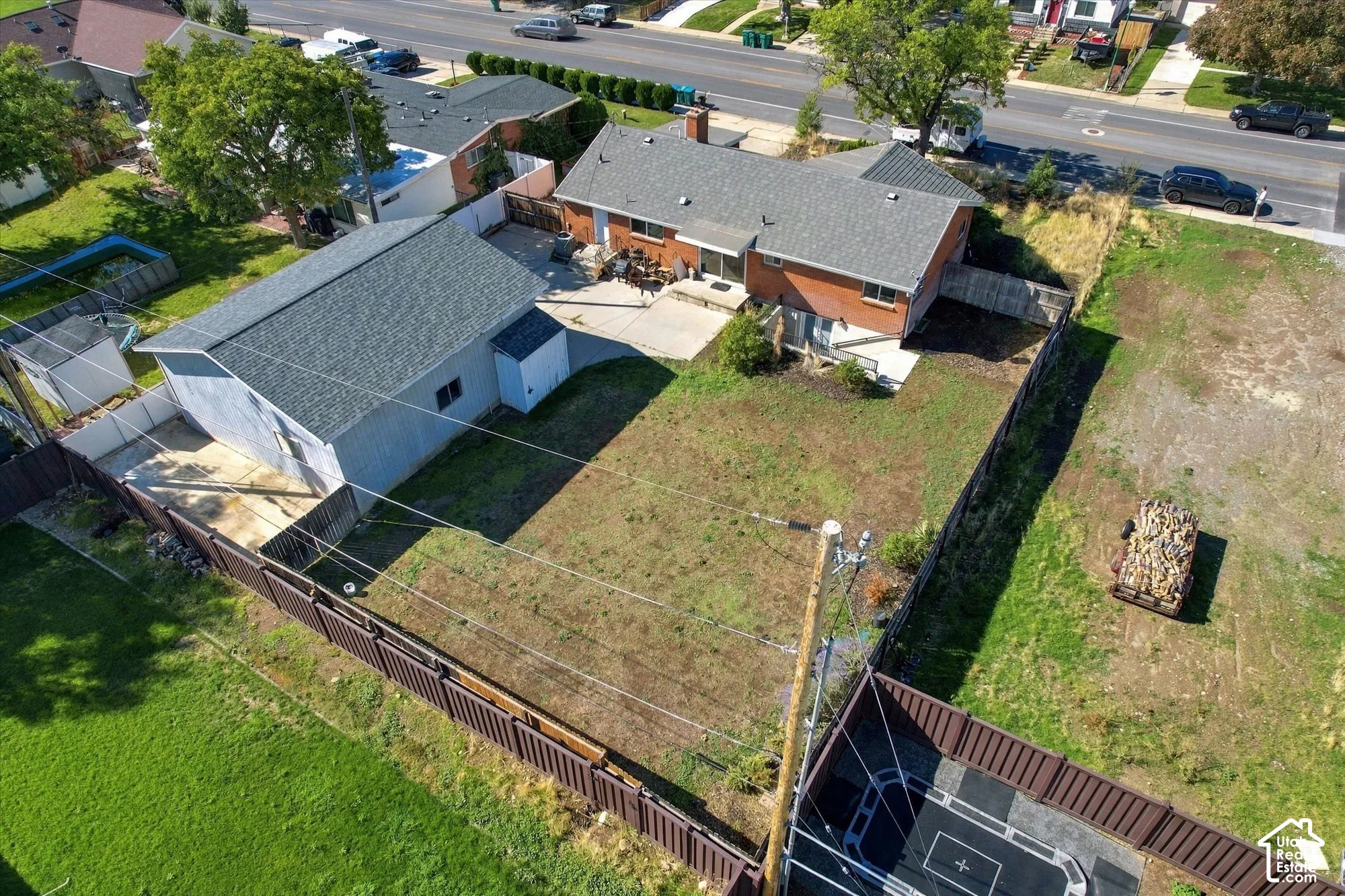 Aerial perspective of a detached residential property featuring a brick and siding exterior, a multi-car detached garage, a concrete patio, and a fully fenced perimeter
