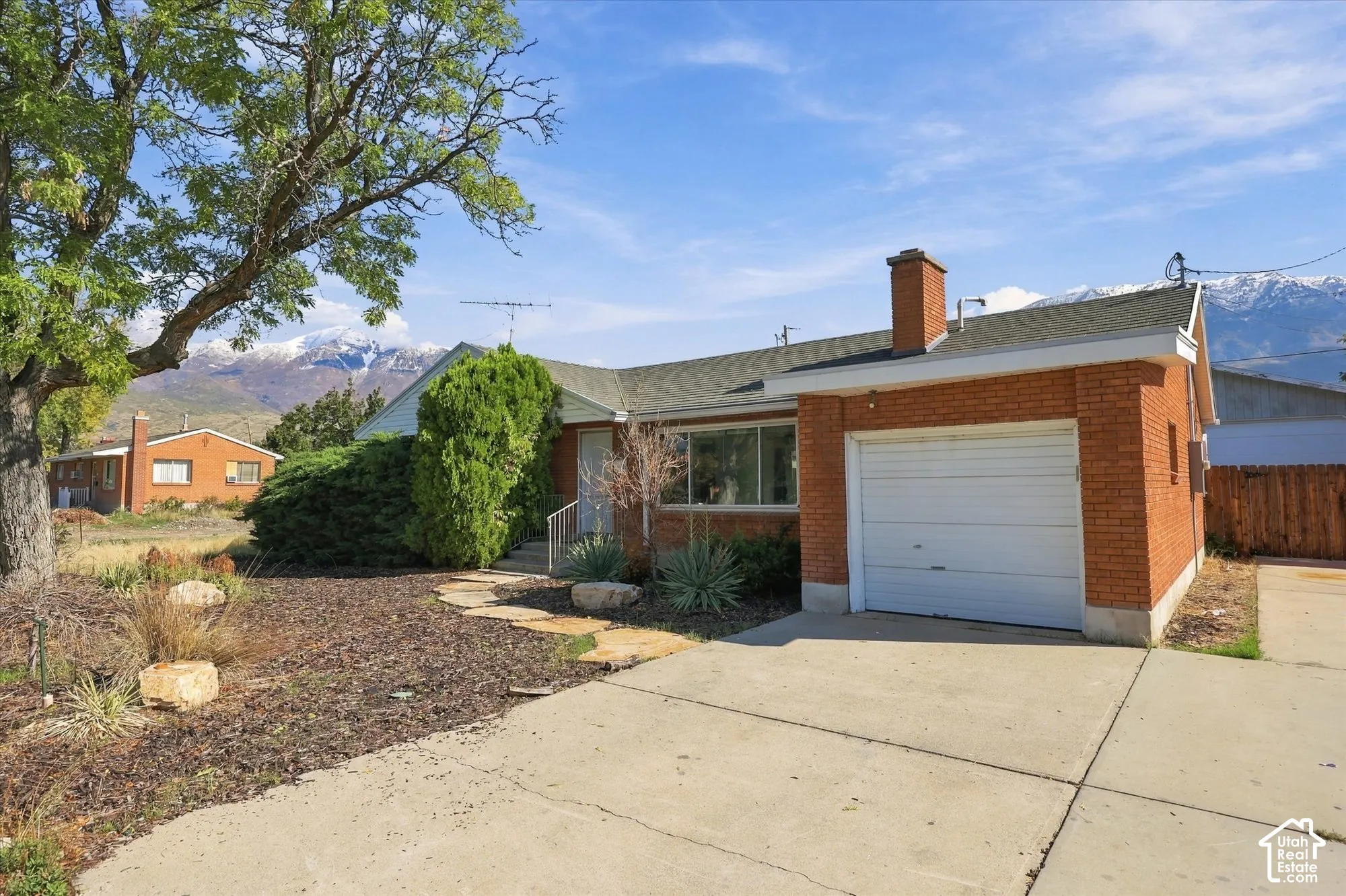 Brick exterior residence featuring an attached garage, concrete driveway, stone walkway, and mountain backdrop