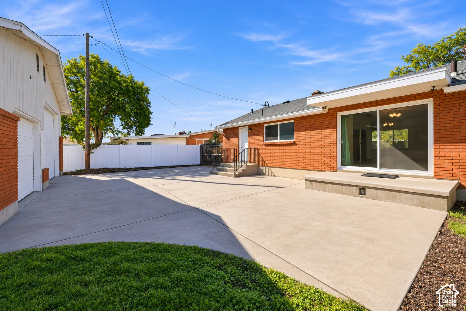 Exterior red brick facade featuring a concrete patio, sliding glass door, detached garage, and white vinyl privacy fencing