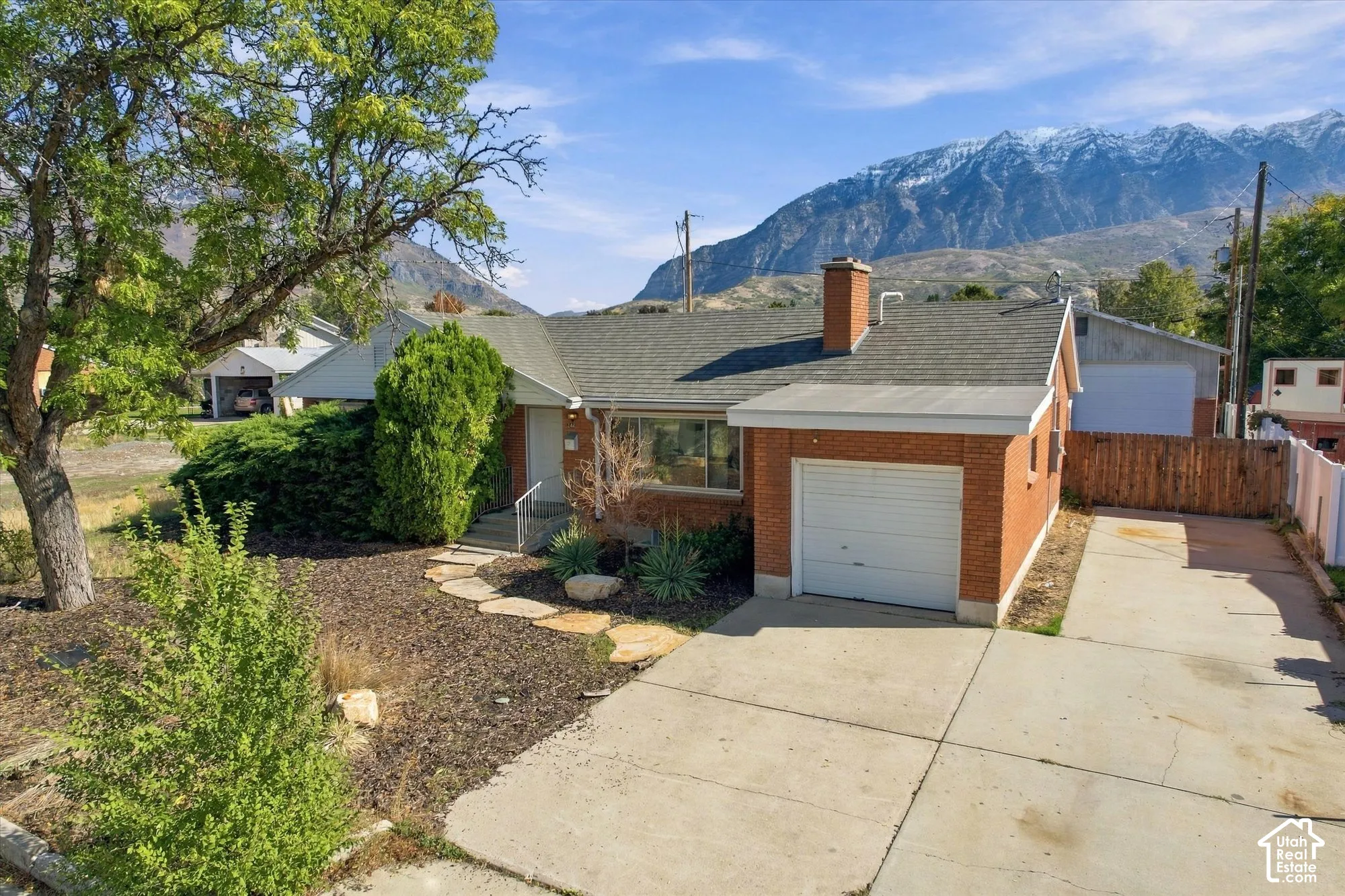 Single-level brick residence featuring an attached garage, paved driveway, flagstone pathway, and mountain backdrop