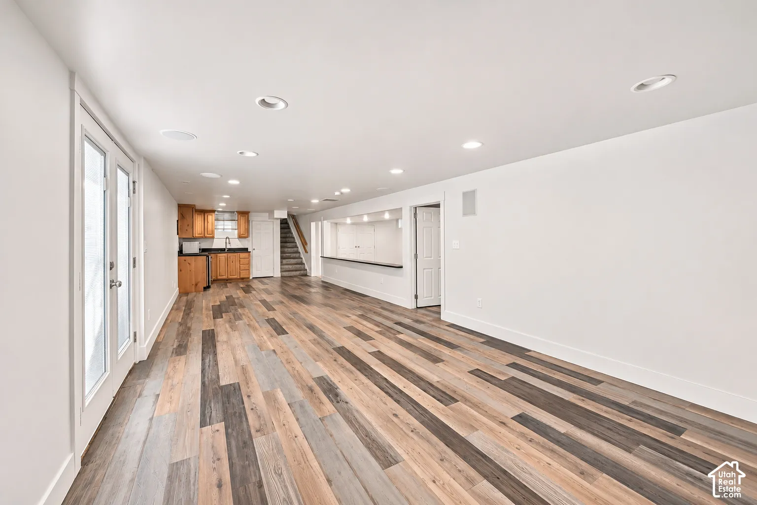 Multi-tone wood-finish flooring, recessed lighting, kitchenette with wood cabinetry, and a built-in refreshment bar featuring a stone-surface countertop
