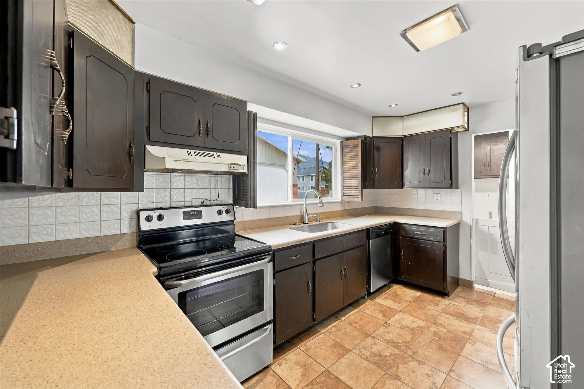 Kitchen featuring dark wood cabinetry, solid-surface countertops, stainless steel electric range, square-tile backsplash, and tiled flooring