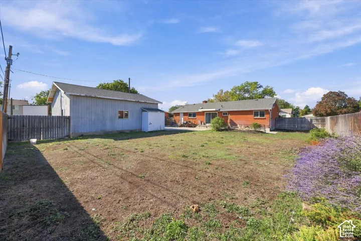 Expansive backyard featuring a brick exterior, detached structure, wood fencing, and established flowering vegetation