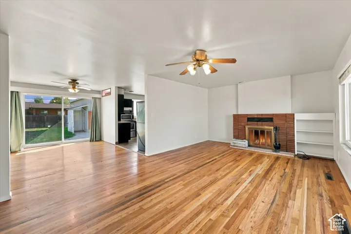 Interior space featuring wood-finish flooring, a floor-to-ceiling brick fireplace with a metal insert, built-in shelving, two ceiling fans, and a large sliding glass door