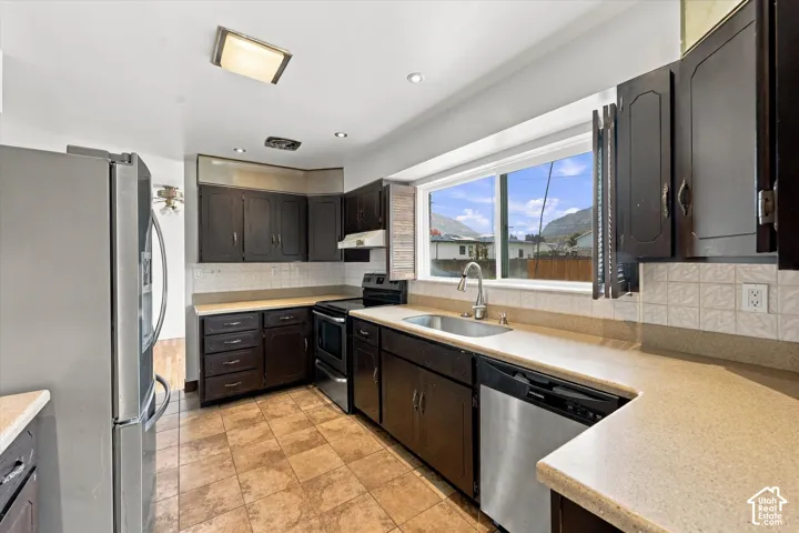 Kitchen featuring dark-finish cabinetry, neutral solid-surface countertops, tile flooring, stainless steel appliances, and a window with a mountain backdrop