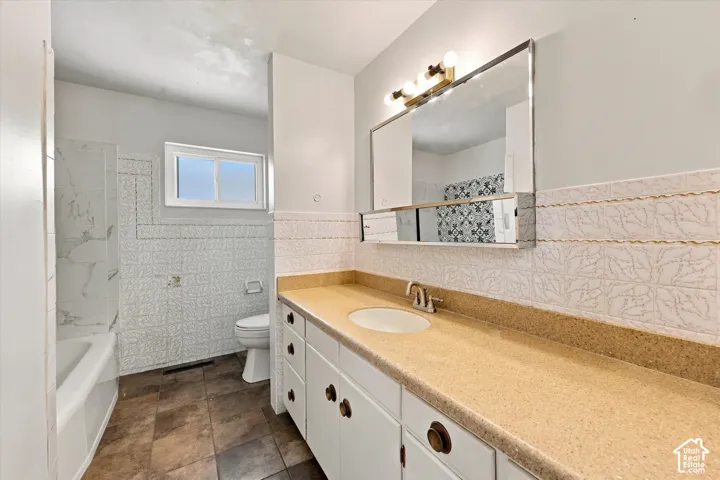 Full bathroom featuring a white vanity with a solid-surface countertop, an integrated sink, a wall-mounted medicine cabinet with a built-in light fixture, tile wainscoting, and a porcelain tub with tile surround
