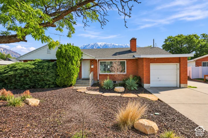 Single-story residence featuring a brick exterior, shingled roof, attached one-car garage, stone walkway, and a mountain backdrop