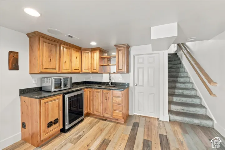 Kitchenette featuring wood cabinetry, stone-finish countertops, integrated beverage refrigerator, recessed lighting, and wood-finish flooring