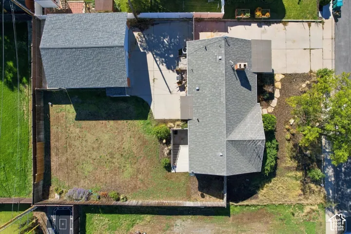 Aerial perspective featuring a detached garage, concrete driveway, fenced yard, and shingled roof